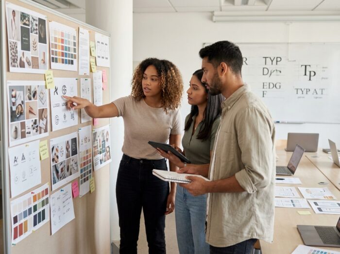 Groupe d'étudiants en design graphique lors d'une séance de critique de projets autour d'un mur de moodboards dans une école de design