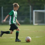 Jeune footballeur adolescent en maillot vert dribblant un ballon sur un terrain municipal français lors d'un entraînement de club