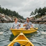 Couple faisant du pédalo sur une baie bretonne aux eaux calmes avec des rochers de granite en arrière-plan
