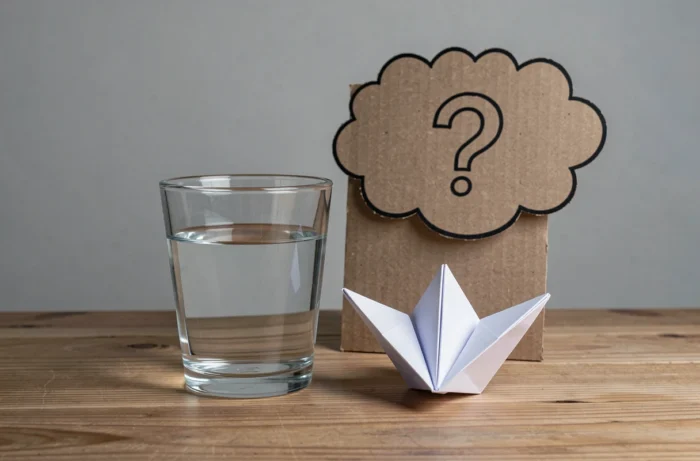 Verre d'eau et cocotte en papier sur une table en bois avec un point d'interrogation en carton